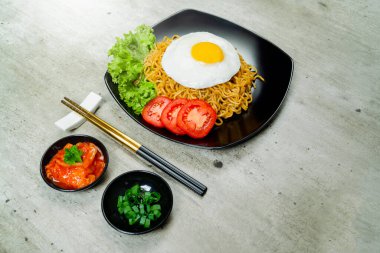 Üstünde yumurta ve domates dilimi olan bir tabak hazır şehriye. Tabak yemek çubukları ve bir kase sosla bir masanın üzerinde.