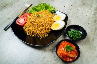 Üstünde domates ve yumurta olan bir tabak hazır şehriye. Tabak yemek çubukları ve kâselerle bir masaya konmuş.