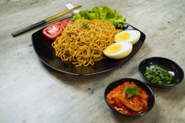 Üstünde domates ve yumurta olan bir tabak hazır şehriye. Tabak yemek çubukları ve kâselerle bir masaya konmuş.