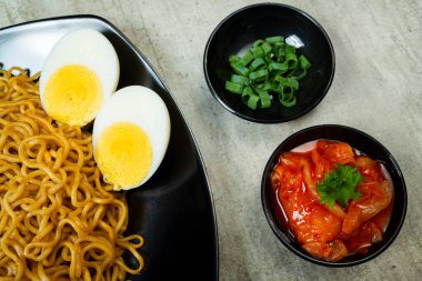 Üstünde domates ve yumurta olan bir tabak hazır şehriye. Tabak yemek çubukları ve kâselerle bir masaya konmuş.
