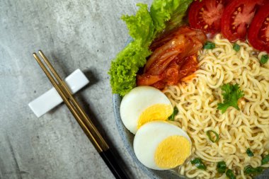 Yumurta ve domatesli bir kase hazır şehriye. Kase yanında çubuklarla birlikte bir masanın üzerinde.