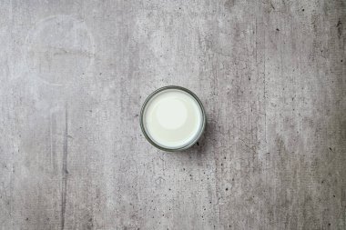 Gri bir yüzeyde bir bardak süt duruyor. Bardağın yarısı dolu ve süt beyaz.