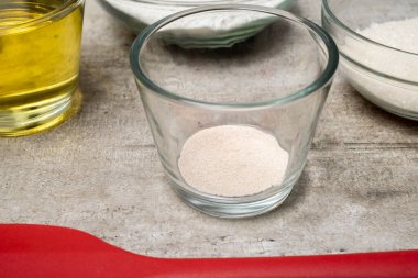 İçinde maya olan cam bir kase diğer kaseler ve şişenin yanındaki masada oturur.