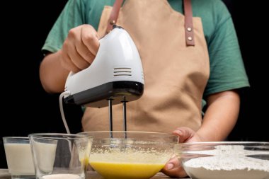 Bir kişi pasta yapıyor ve masanın üzerinde bir kase un ve şeker var. Malzemeleri karıştırmak için karıştırıcı kullanıyor.