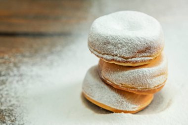 Üst üste istiflenmiş üç pudra çöreği. Çörekler pudra şekerle kaplanmış ve taze yapılmış gibi görünüyor. Hoşgörü ve keyif kavramı