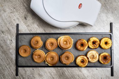 Çörek tepsisi tezgahın üzerinde tost makinesinin yanında duruyor. Çörekler çeşitli şekil ve boyutlarda ve hepsi kahverengi. Sıcaklık ve rahatlık kavramı