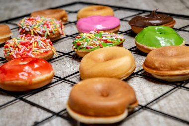 Bir tepsi çeşitli mini donutlar, şekerli ve şekerli. Mini çörekler farklı renkte ve tatlarda ve şebeke şeklinde dizilmiş. Çeşitlilik ve bolluk kavramının yanı sıra oyuncu bir...