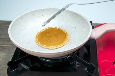 Fırının tepsisinde krep pişiriliyor. Gözleme, bir spatulayla çevrilme aşamasında.