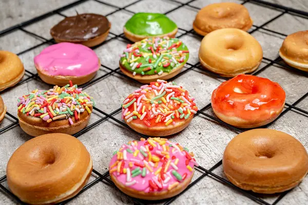 Bir tepsi çeşitli mini donutlar, şekerli ve şekerli. Mini çörekler farklı renkte ve tatlarda ve şebeke şeklinde dizilmiş. Çeşitlilik ve bolluk kavramının yanı sıra oyuncu bir...