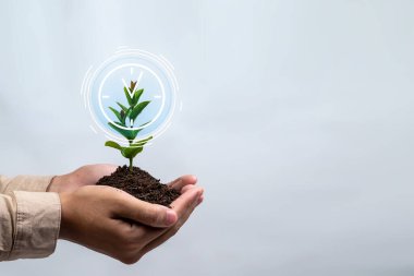 Bir insan elinde bir bitki tutuyor, topraktan çıkan bir bitki. Resmin arka planında zamanın geçtiğini gösteren bir saat var. Sahne büyüme ve değişimin bir parçasıdır.