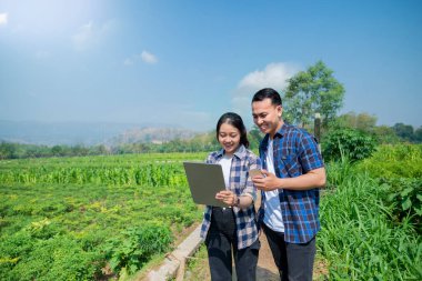 Bir adam ve bir kadın tarlada bir tablete bakıyorlar.