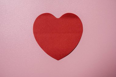 Kırmızı kalp pembe arka plandadır. Kalp kağıttan yapılır ve pembe yüzeyin üzerine yerleştirilir.