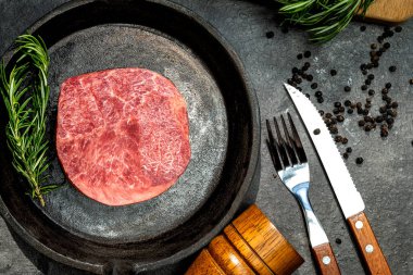 Yanında çatal ve bıçak olan bir tavada fileto eti var. Fileto çiğ ve üzerinde çok baharat var.
