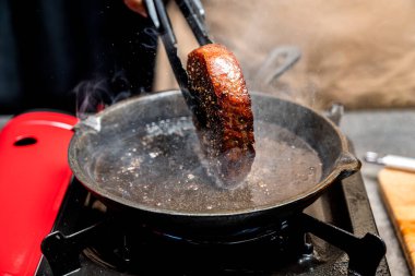 Birisi fırında tavada fileto biftek pişiriyor.