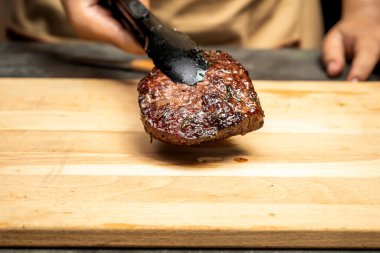 Bir insan ahşap kesme tahtasının üzerinde fileto eti tutuyor. Et kahverengidir ve pişmiştir.
