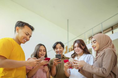 Bir grup Endonezyalı birlikte cep telefonlarına bakıyor. Hepsi gülümsüyor ve eğleniyor gibi görünüyorlar.