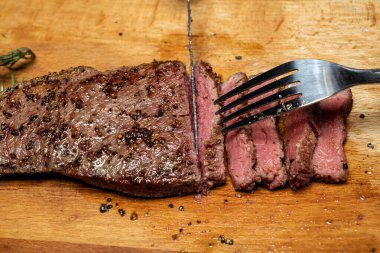 Bir insan, tahta bir kesme tahtasına çatal ve bıçakla Picanha eti kesiyor.