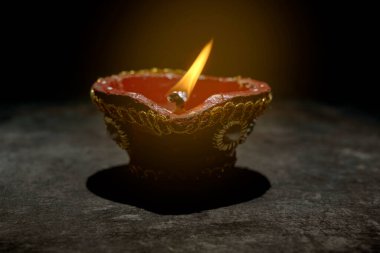 Mavi ve beyaz desenli kırmızı ve altın madalyalı bir tencere koyu bir yüzeyde duruyor. Tencerenin içinde küçük bir alev yanıyor. Diwali konsepti