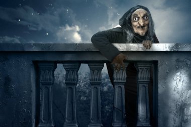 Balustrade 'ın arkasından ay ışığında yükselen yaşlı cadı. Manzara korkutucu ve ürkütücü. Ürkütücü Cadılar Bayramı konsepti