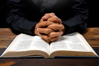 Elleri açık kutsal bir İncil 'in üzerinde ahşap masada dua eden bir adam. İnancın ve Tanrı 'ya tapmanın sembolü. Kilisedeki insanlar Hıristiyanlık duası. Dini hizmet, tatil veya konsept