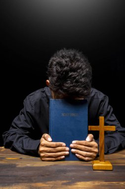 Din haçı ve kutsal İncil ile tahta masada dua eden bir adam. İnancın ve Tanrı 'ya tapmanın sembolü. Kilisedeki insanlar Hıristiyanlık duası. Dini hizmet, tatil veya konsept
