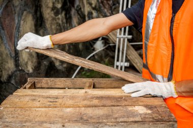 Yelekli ve eldivenli işçiler palet parçalarını söküyorlar. Sahne deponun arka planında geçiyor. Ahşap fabrikası