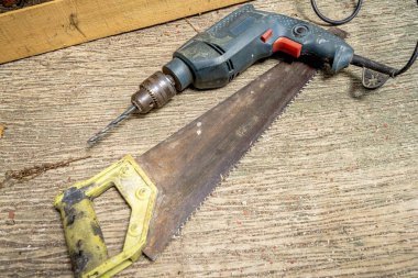 Beton zeminde oturan el testeresi ve elektrikli matkabın yakın görüntüsü. İnşaat ve marangozluk konsepti