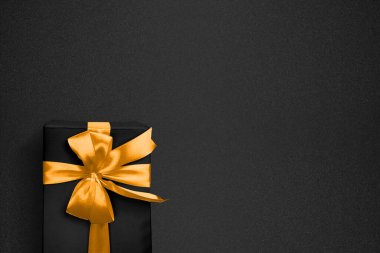 Siyah arka planda desenli altın bir fiyonk ile süslenmiş siyah hediye kutusu. Uzayı kopyala Model ya da şablon. Doğum günü, yıldönümü hediyeleri, hediye kartpostalları. Düz yatıyordu