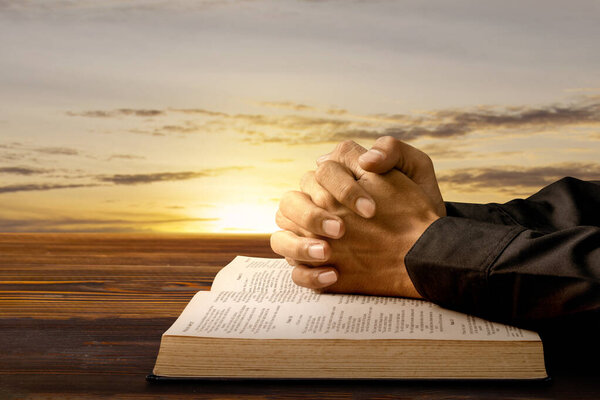 Man praying with his hands on a opened holy bible on wooden table. Symbol of faith and worship in God. People christianity prayer. Religious service, holiday or concept