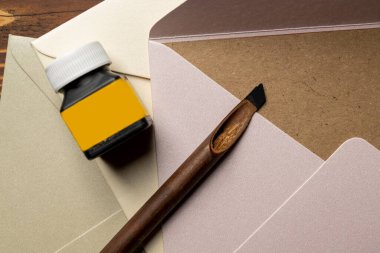 Kaligrafi kamışları mürekkeple kaplıydı. Masada mürekkep, zarf ve kahverengi kart yığını vardı. Modelleme. Uzayı kopyala Arapça yazı yazmak için sazlıklar kalem mürekkebi