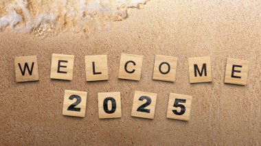 Plajdaki kum arka planında 2025 yazısıyla tahta küpleri. Mutlu yıllar konsepti ya da kutlama