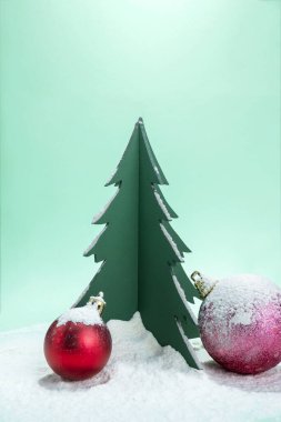 Noel ağacı minyatürünün ve renkli arkaplanda karla kaplı Noel toplarının yakın görüntüsü. Noel kutlaması için dekorasyon