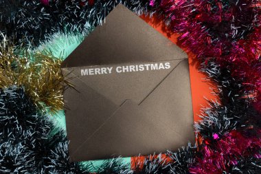 Renkli bir arkaplanda Noel süsü çerçevesi olan bir zarfın üzerindeki Mutlu Noeller metninin yakın görüntüsü. Noel kutlaması için dekorasyon