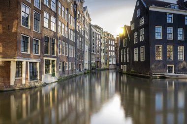 Amsterdam, Hollanda 'da güneş ışığı arka planında nehir kanalına yansıyan renkli Amsterdam evlerinin cephelerinin panoramik görüntüsü