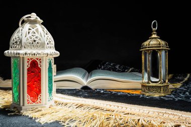 Arap fenerleri ve Kur 'an, siyah arkaplanı olan bir dua örtüsü üzerinde. Müslüman bayramı kutlaması için dekorasyon. İslami oruç, Ramazan Kareem, Kurban Bayramı, Kurban Bayramı veya Mübarek selamlar