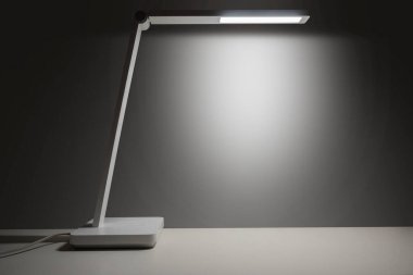 Beyaz masa lambası, beyaz masayı koyu bir arka planda aydınlatıyor. Uzayı kopyala Model, çalışma ya da çalışma alanı şablonu