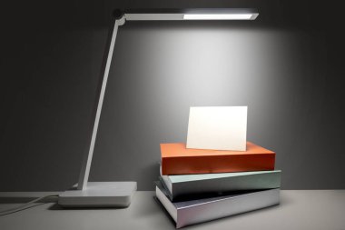 Beyaz masa lambası aydınlatma kartı beyaz bir masanın üzerindeki kitap yığınının üzerinde koyu bir arka planda. Uzayı kopyala Model veya çalışma alanı şablonu