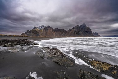 Siyah kumlu Vestrahorn Dağı 'nın panoramik manzarası ve Stoksnes, İzlanda kıyıları. Doğa, seyahat, kış arkaplanı veya duvar kağıdı