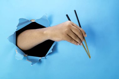 Bir insan eli yırtık bir kağıdı ahşap bir çubukla tutuyor. El hareketleri yiyeceğe ulaşmak ya da kapmak için. Boşluk oluştur ya da kopyala