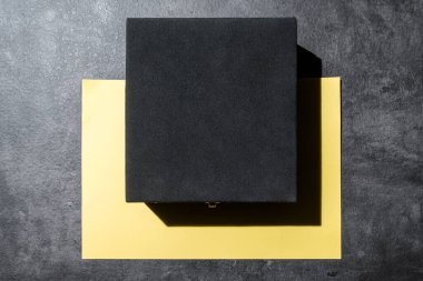 Siyah hediye kutusunun üst görüntüsü ve masanın üzerindeki boş kağıt. Model ya da kopyalama alanı. Tatiller, yıldönümleri, kutlamalar, hediyeler ya da sürprizler için dekorasyon kavramı. Düz yatıyordu