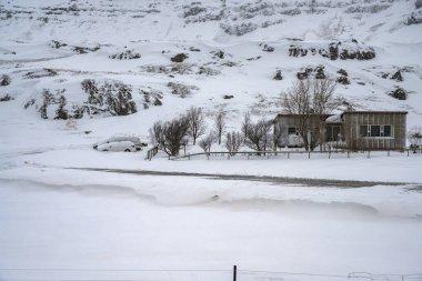 İzlanda 'da karla kaplı tarlalar ve dağlarla kaplı ev manzarası. Doğa, seyahat, kış arkaplanı veya duvar kağıdı