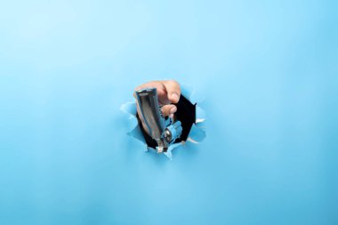 İnsan eli tabancayı yırtılmış kağıdın içinden tutuyor. El hareketleriyle. Model veya Kopyala uzayı. Silahları, savaşı, suçu veya şiddeti hedeflemek