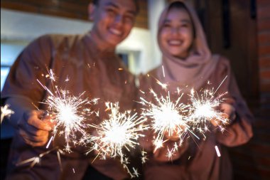 Asyalı Müslüman bir çift memlekette havai fişek gösterisi yapıyor. Kurban Bayramı, İdul Fitri, Lebaran ve Ramazan Mübarek kutlamaları