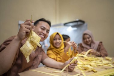 Endonezyalı Müslüman aile, genç hindistan cevizi yapraklarından ketuplu pirinç köftesi dokuyorlar. Geleneksel Müslüman yemekleri, Mutlu Lebaran, Kurban Bayramı, Idul Fitri ve Ramazan Mübarek kutlamaları sırasında