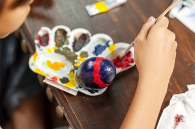 Endonezyalı güneydoğu Asyalı küçük kız masanın üzerinde paskalya yumurtası süslemesi için fırçayla bir yumurta boyuyor. Paskalya bayramını kutlama kavramı