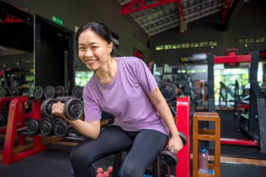 Çinli Doğu Asyalı kadın spor salonunda dambıl kaldırırken spor yapıyor. Spor salonu ve sağlıklı yaşam tarzı konsepti