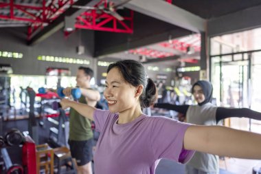 Çinli Doğu Asyalı ve Arap Ortadoğu Müslüman kadın Endonezyalı güneydoğu Asyalı erkek spor salonunda halteri gererken ve kaldırırken spor yapıyor. Spor salonu ve sağlıklı yaşam tarzı konsepti