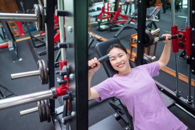 Çinli Doğu Asyalı kadın spor salonunda göğüs pres makinesi eğitimi alıyor. Spor salonu ve sağlıklı yaşam tarzı konsepti