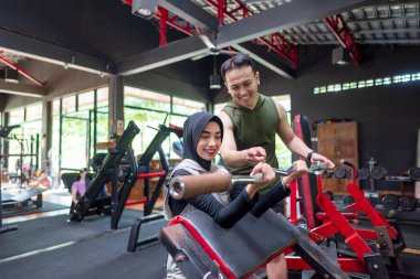 Arap Ortadoğulu Müslüman kadın spor salonunda Endonezyalı güneydoğu Asyalı bir antrenörle göğüs presi eğitiminde. Spor salonu ve sağlıklı yaşam tarzı konsepti