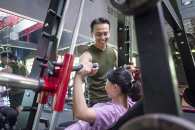 Çinli Doğu Asyalı kadın spor salonunda Endonezyalı bir Güneydoğu Asyalı antrenörle göğüs pres makinesi eğitimi alıyor. Spor salonu ve sağlıklı yaşam tarzı konsepti